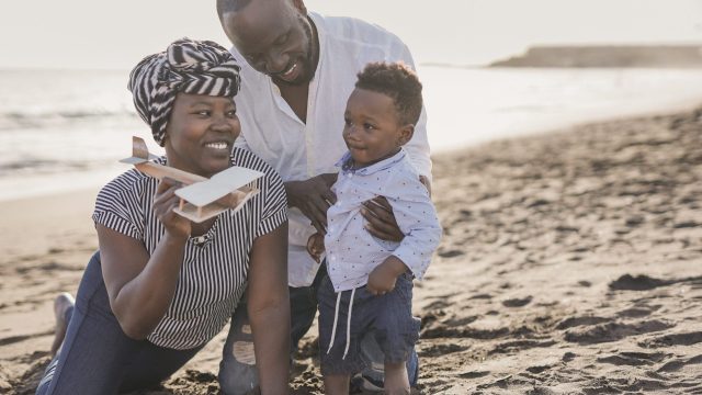 Happy african family having playful time on the beach - Family love - Parents and toddler outdoor